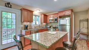 Cucina con mobili in legno, elettrodomestici in acciaio inossidabile, piano di lavoro in granito e vista sull'esterno.