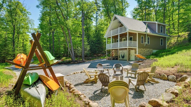 Una casa a due piani con un balcone, circondata da un patio di ghiaia con poltrone Adirondack e kayak.