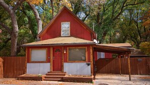 A red wooden house with a front porch, a garage, and a fenced yard.