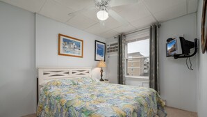 A bedroom with a bed, a lamp, a TV, and a window with curtains. - Oceanfront condos with 3 night minimum rentals and linens included! (Ocean City)