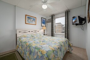 A bedroom with a bed, a lamp, a TV, and a window with curtains.