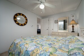 A bedroom with a bed, a ceiling fan, a round mirror, a dresser, and a lamp.