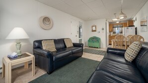 A living room with a black leather sofa, a small table with a lamp, and a green rug. - Oceanfront condos with 3 night minimum rentals and linens included! (Ocean City)