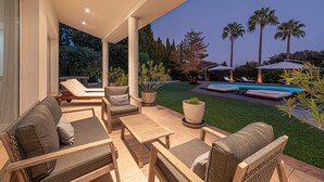 Uma área de pátio com mobiliário externo, piscina e palmeiras.