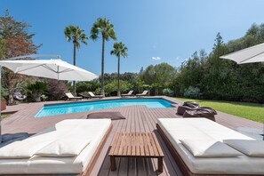A poolside area with lounge chairs, a wooden deck, and palm trees.