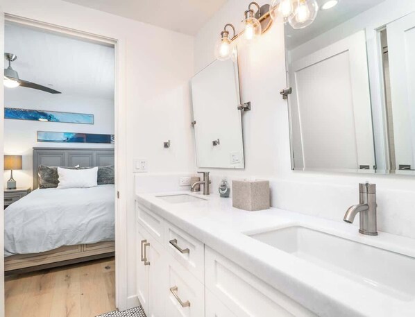 A modern bathroom with a double sink, large mirrors, and a ceiling fan.