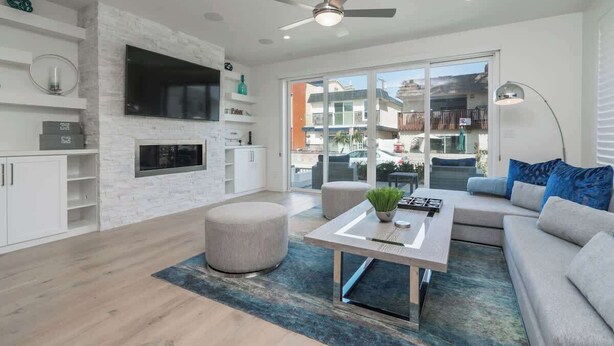 Un salon moderne doté d’un téléviseur à écran plat, d’un ventilateur de plafond, d’un canapé, de poufs et d’une table basse.