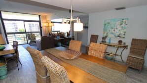Un vaste espace dédié à la salle à manger, avec une longue table en bois, des chaises en osier et une grande fenêtre offrant une vue sur le paysage urbain.