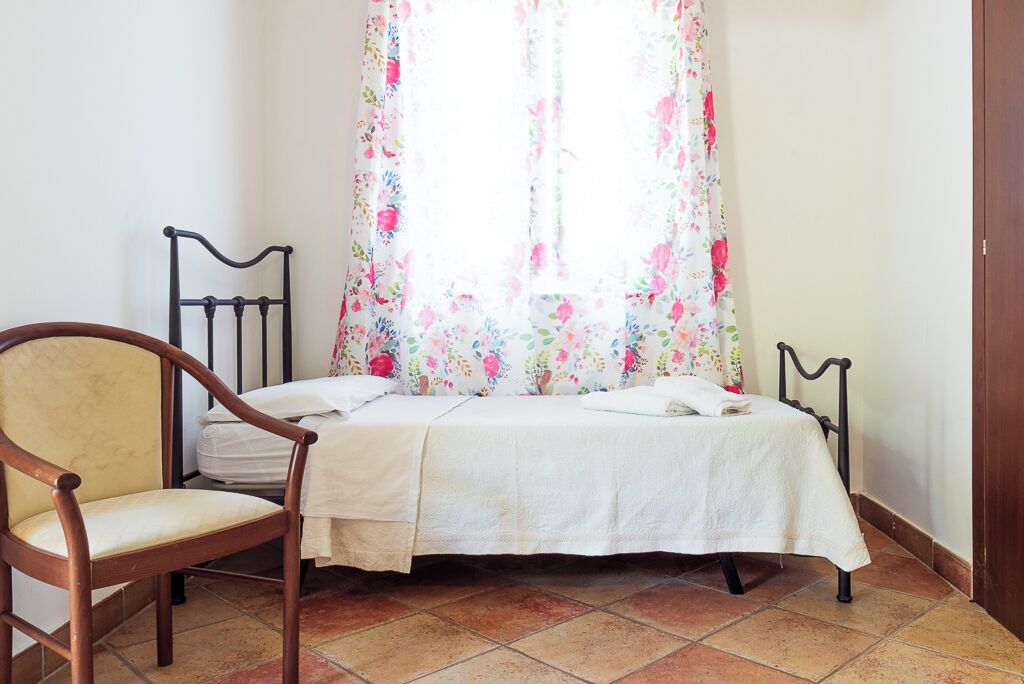 Une chambre à coucher avec un lit, deux chaises et une fenêtre ornée de rideaux à motifs floraux.