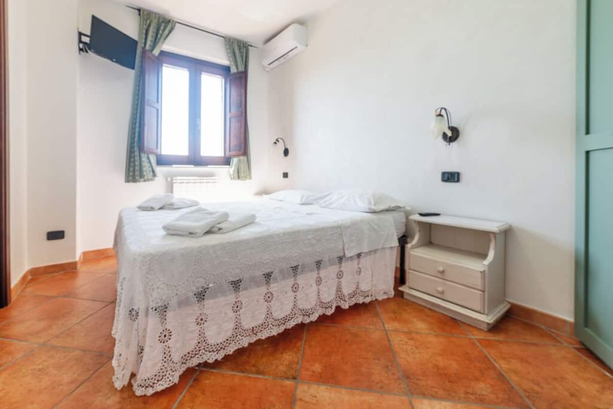 Un dormitorio con cama, mesita de noche, cortinas en la ventana y un equipo de aire acondicionado.