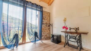 Una habitación con un ventanal grande, una máquina de coser sobre una mesa de madera y una pared de piedra.