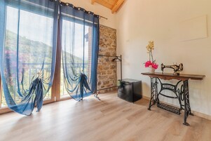 Una habitación con un ventanal grande, una máquina de coser sobre una mesa de madera y una pared de piedra.