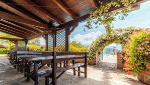 Un espacio de estar al aire libre con techo, bancos de madera y vistas a una piscina.