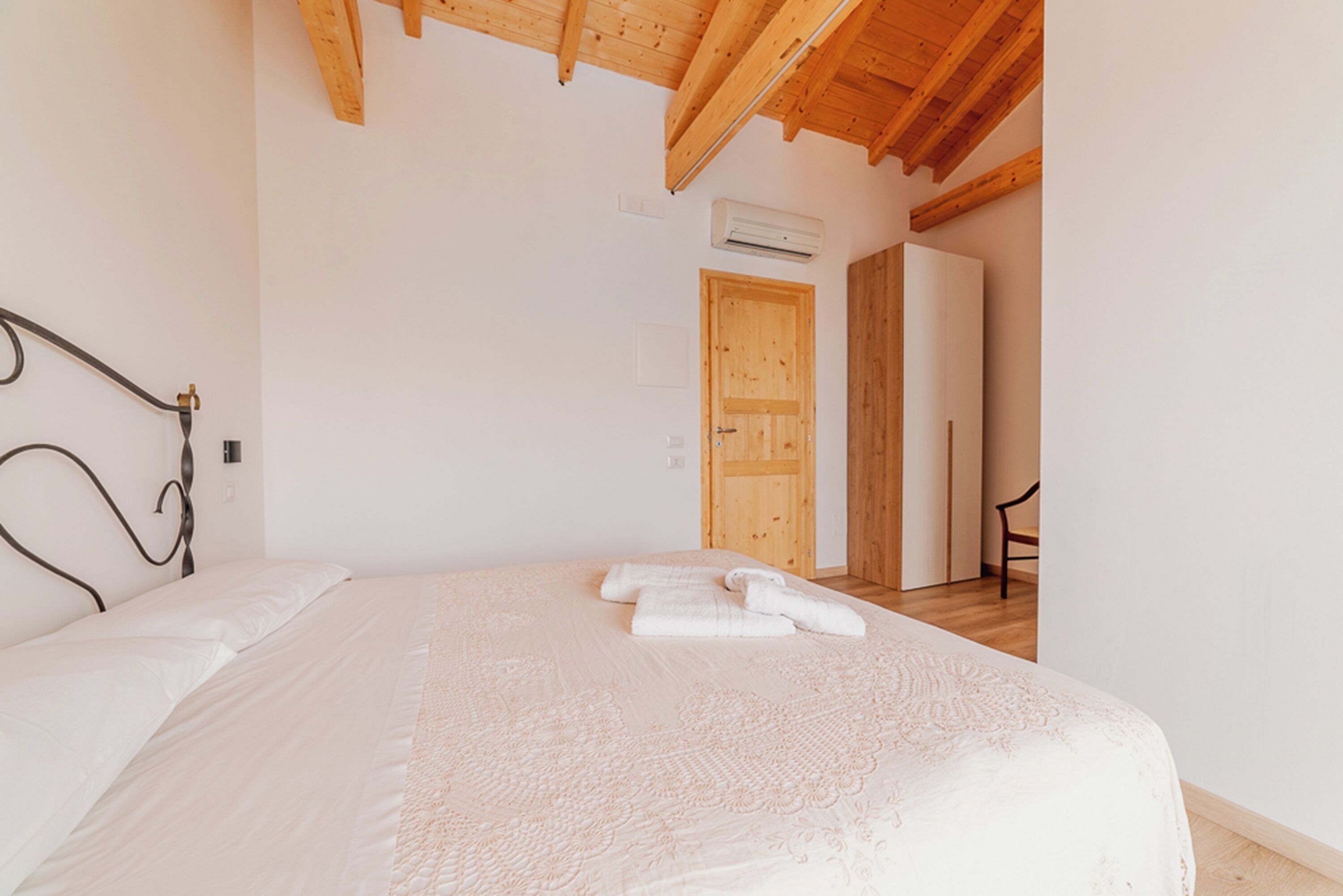 A bedroom with a wooden ceiling, a bed with a white bedspread, and a wooden door in the background.