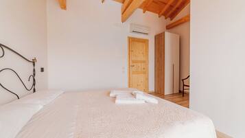 Un dormitorio con techo de madera, una cama con colcha blanca y una puerta de madera al fondo.