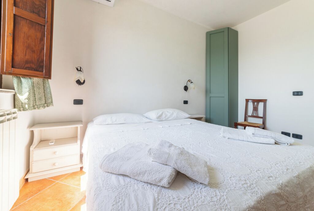 A bedroom with a bed, a wooden wardrobe, a nightstand, and a wall-mounted heater.