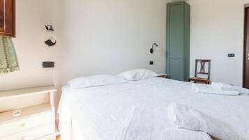 Una cama bien hecha con sábanas y toallas blancas, una mesita de noche, una lámpara de pared y una puerta verde.