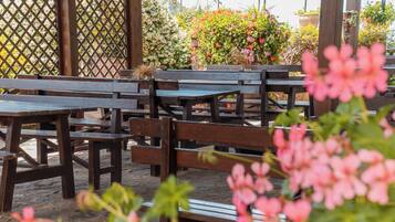 A patio area with wooden benches and tables, surrounded by a lattice fence and various plants.