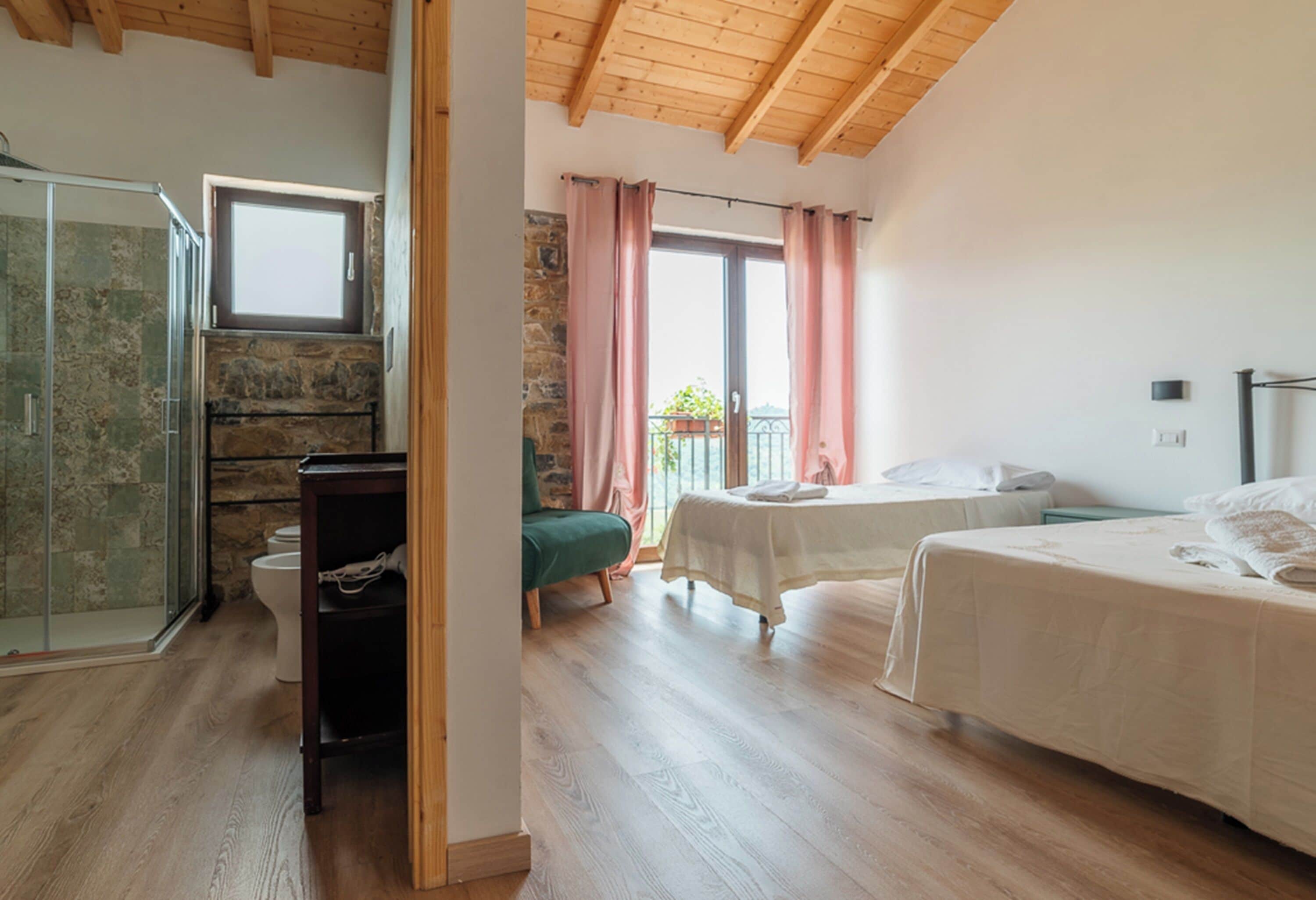 Een slaapkamer met twee bedden, een douche en een balkon met roze gordijnen.