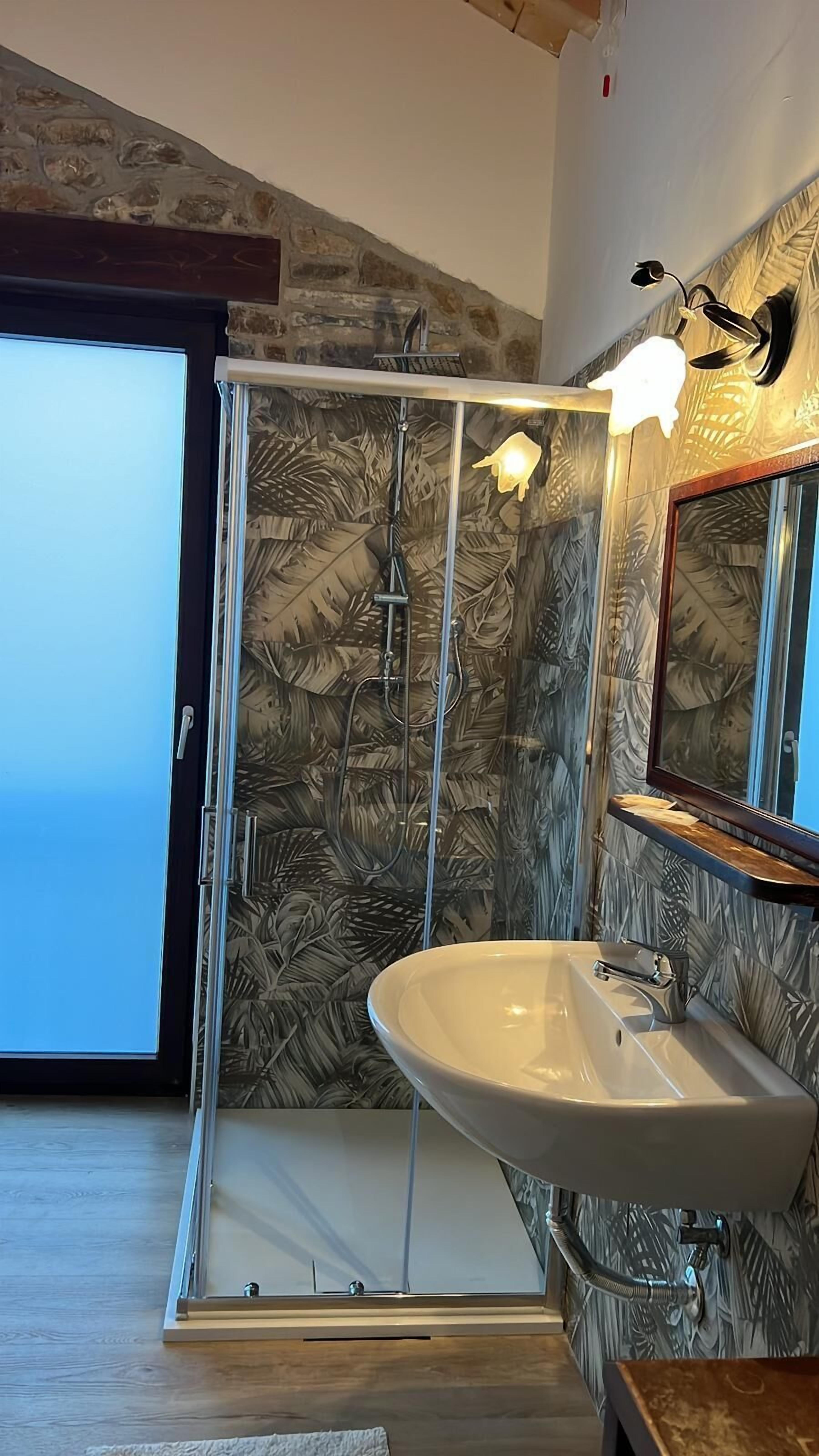 A bathroom with a glass shower enclosure, a white sink, and a mirror with a wooden frame.
