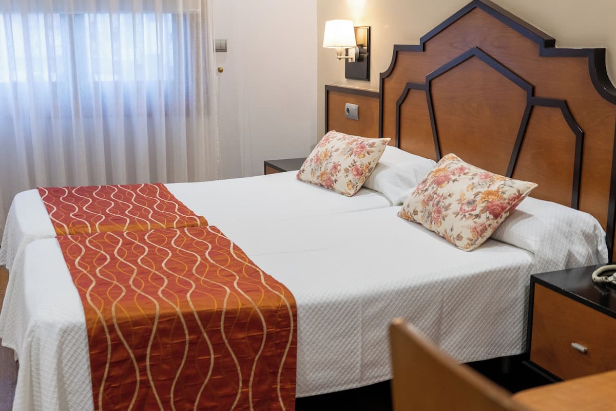 A hotel room with a bed, a nightstand, a telephone, and a wall-mounted lamp.