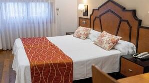 Una habitación de hotel con una cama, una mesita de noche, un teléfono y una lámpara de pared.