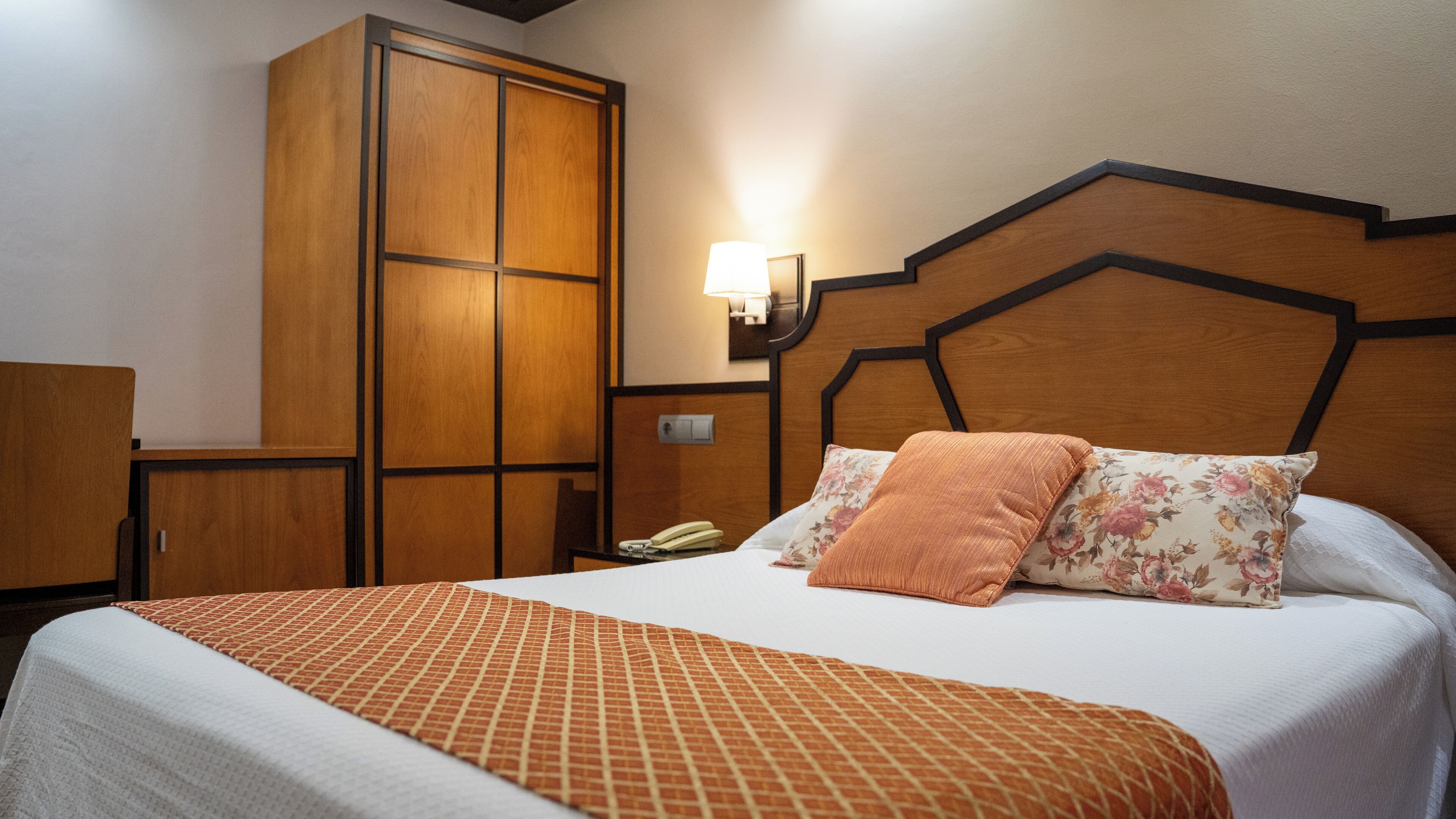 Una habitación de hotel con una cama, un armario, una mesita de noche y una lámpara en la pared.