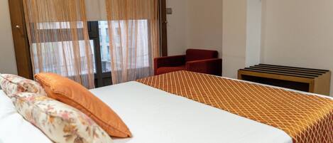 Habitación de hotel con cama, una silla, una mesita y una ventana con cortinas.