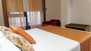 Une chambre d’hôtel avec un lit, une chaise, une petite table et une fenêtre avec des rideaux.