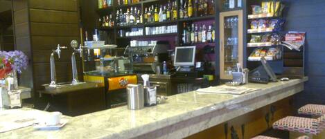 A bar area with a marble counter, stools, shelves with bottles, a computer, and a cash register.
