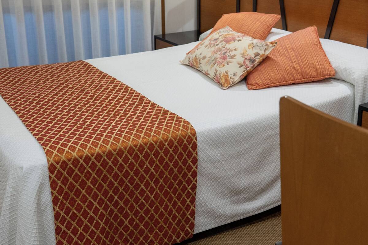 A hotel room with a bed, a nightstand, a lamp, and a chair.
