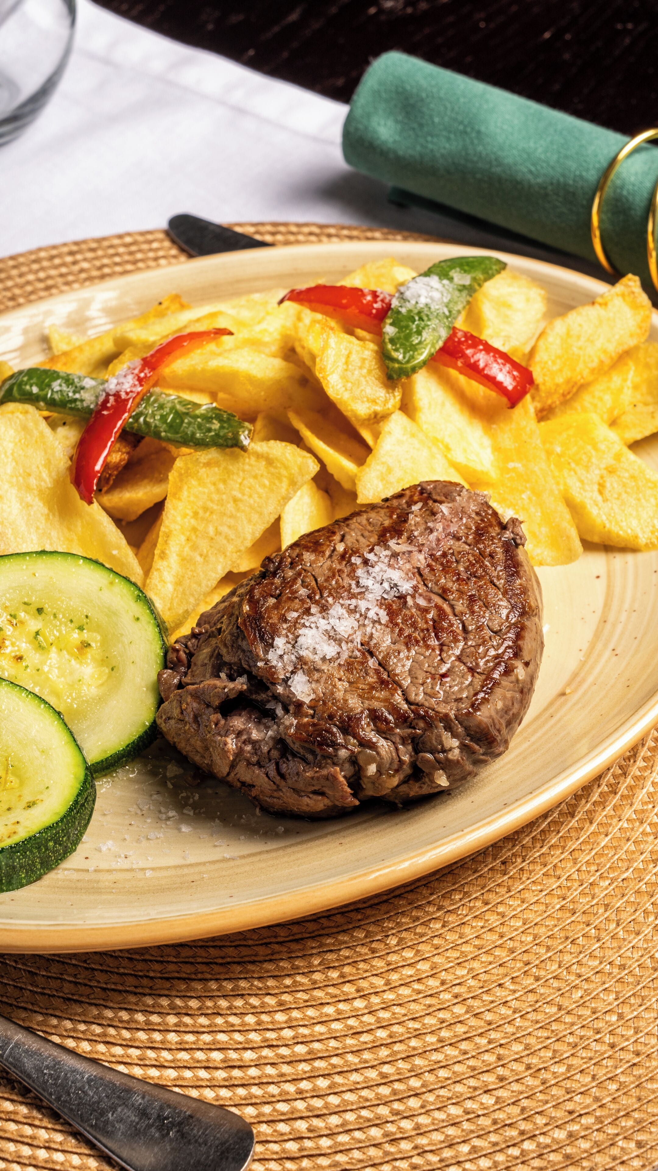 A plate with a steak, fries, and sliced zucchini.