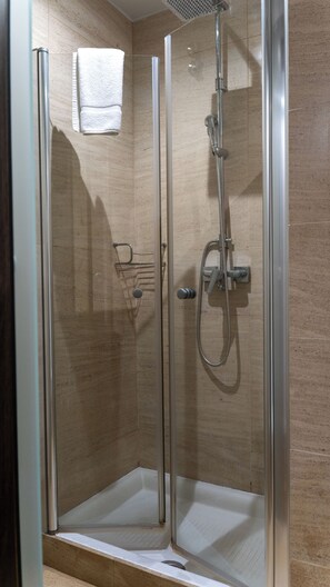Cabina de ducha con paredes de vidrio, cabezal de ducha de mano y grifo empotrado.