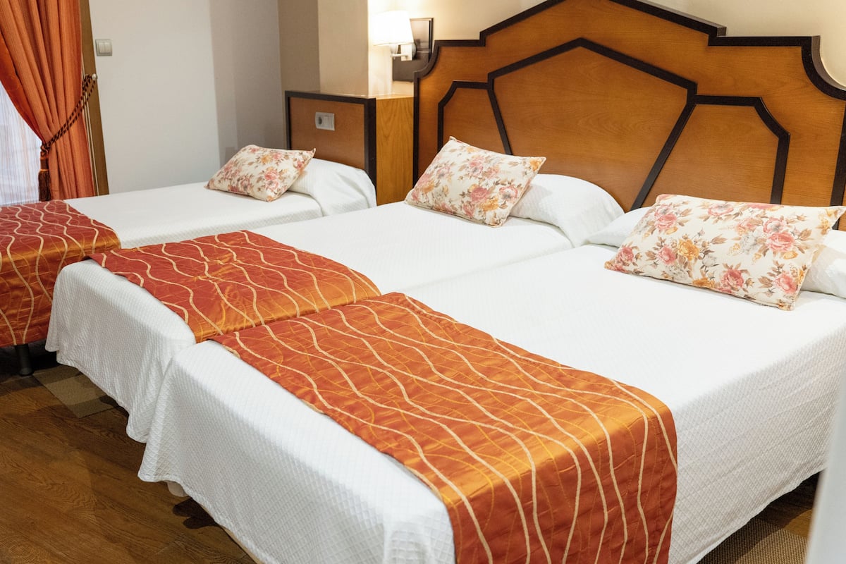 A hotel room with two beds, each with a white bedspread and orange decorative pillows.