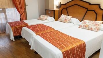 Habitación de hotel con dos camas, cada una con cubrecama blanco y almohadones decorativos naranja.