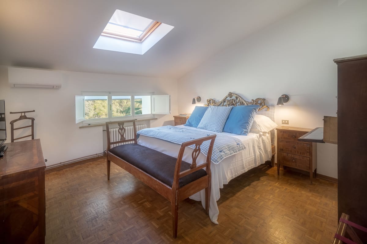 Ein Schlafzimmer mit Dachfenster, Holzboden, einem Bett mit blauer Bettwäsche, einem Nachttisch und einer Kommode.
