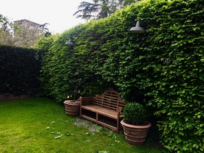 A wooden bench in a lush garden with a hedge and two large planters. - Sottoalfico B&B (Rimini)