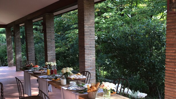 Un área de comedor al aire libre con una mesa dispuesta para cuatro personas, rodeada de pilares de piedra y vistas a exuberante vegetación.