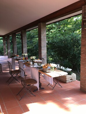 An outdoor dining area with a table set for four, surrounded by stone pillars and a view of lush greenery. - Sottoalfico B&B (Rimini)
