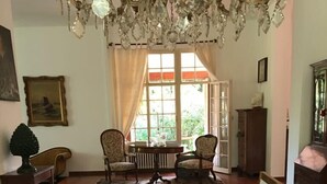 Comedor con una larga mesa dispuesta para una comida, que cuenta con una araña, sillas y vistas al exterior con vegetación.