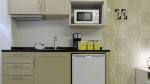 A compact kitchen with a microwave, sink, and a small refrigerator. There are cabinets with handles and a countertop with a coffee maker and labeled containers.