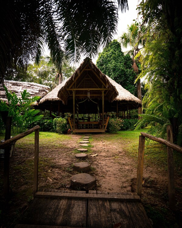A wooden pathway leading to a thatched-roof hut surrounded by lush greenery. - Amak Iquitos Ecolodge (Indiana)