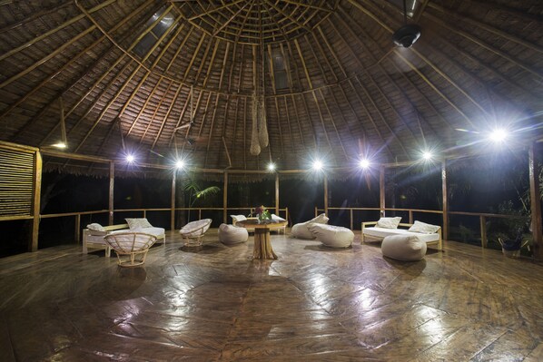 A spacious room with a thatched roof, a central table, and multiple seating areas.