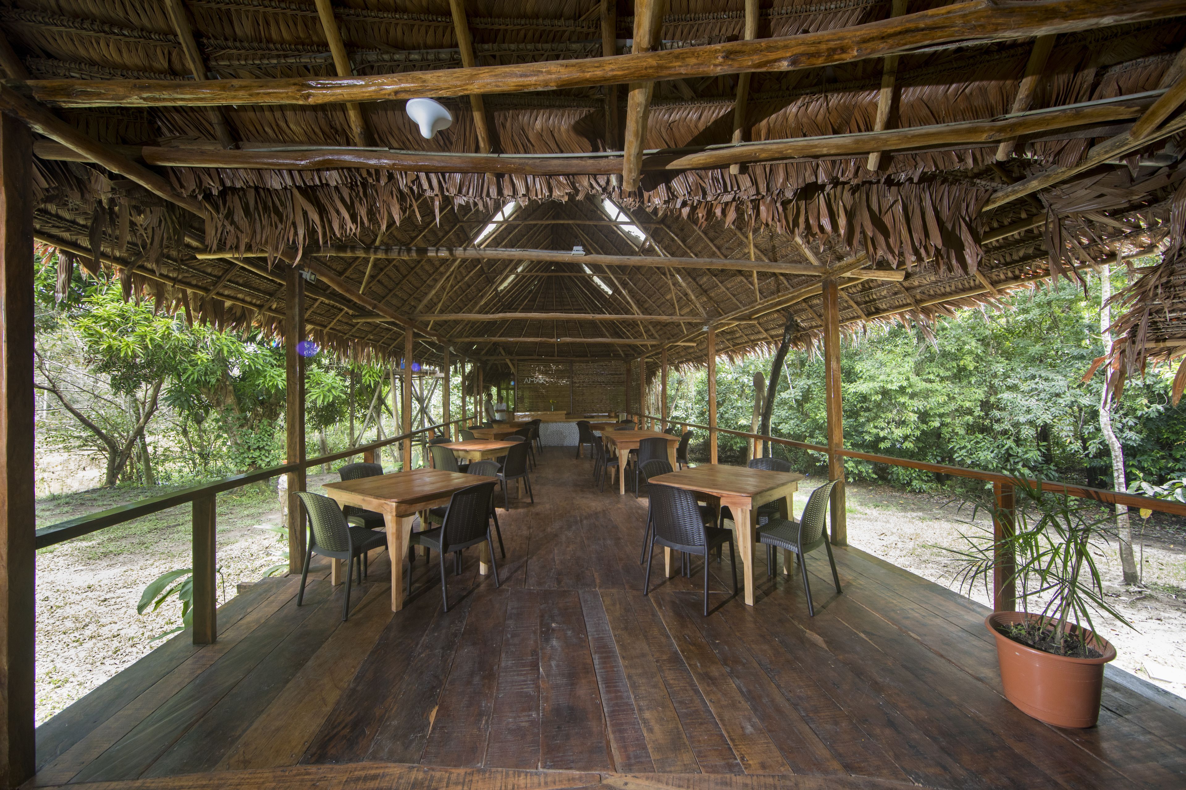 Een terras met houten tafels en stoelen, omringd door een houten dek en een rieten dakconstructie.