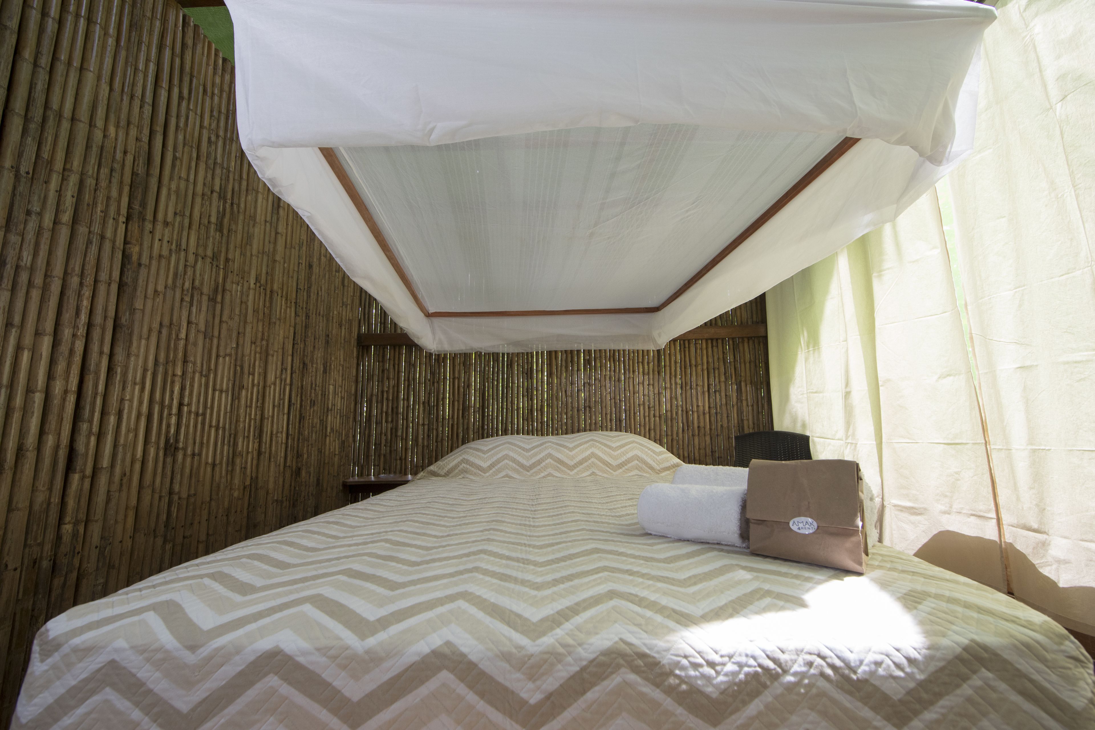 A bed with a chevron-patterned bedspread, a white canopy, and a bamboo wall.