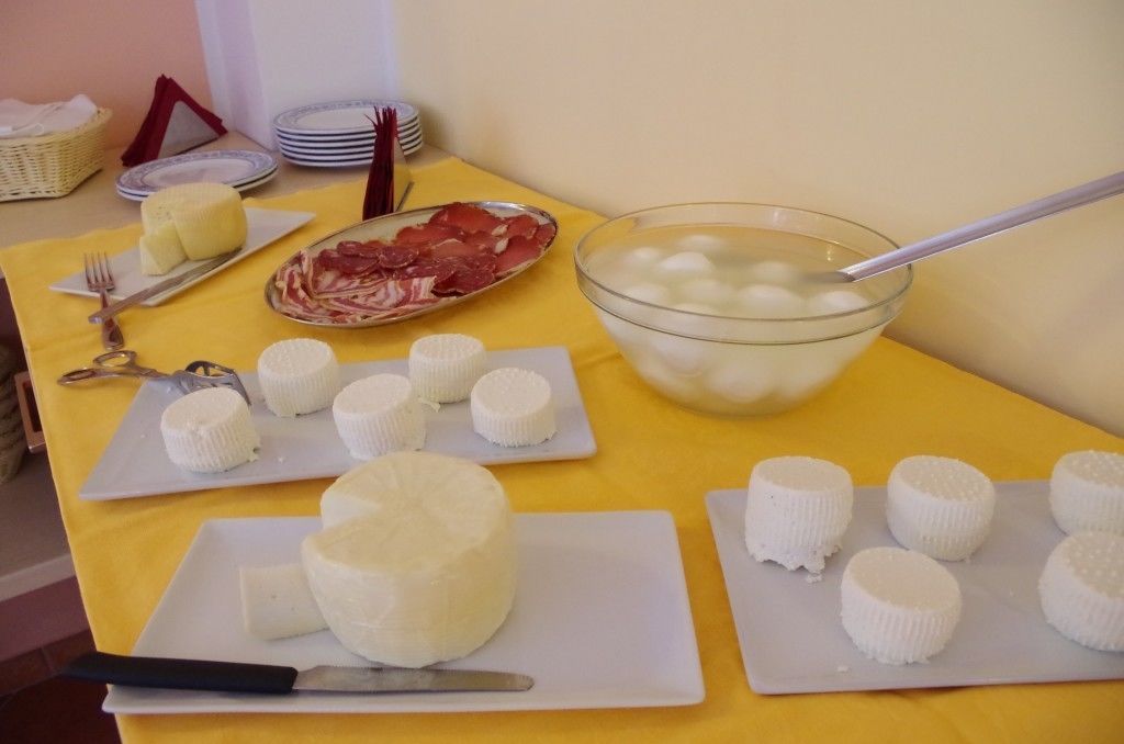 Un tavolo con diversi prodotti lattiero-caseari, tra cui formaggi, salumi e una ciotola di yogurt.