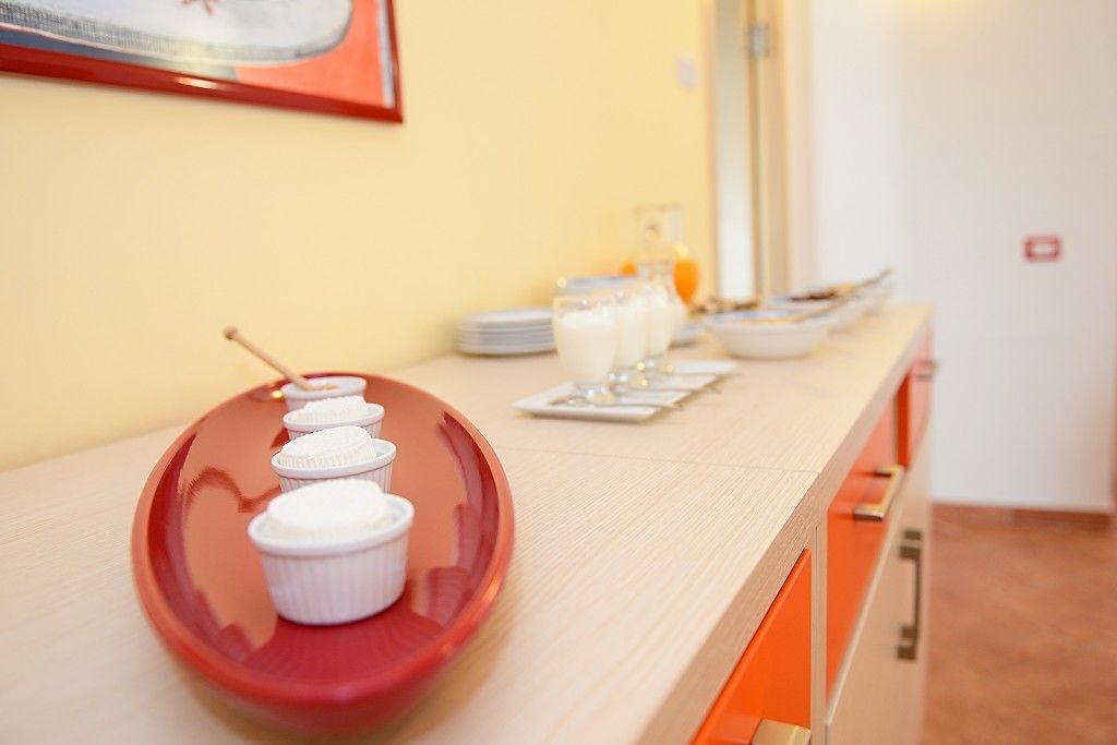 A breakfast buffet setup with a red tray holding several white cups and a glass of orange juice.