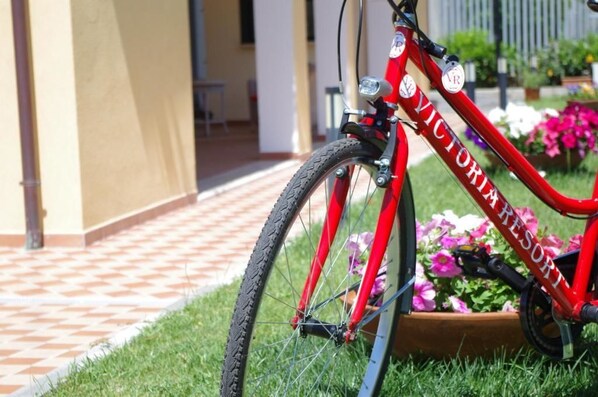 A red bicycle with "VICTORIA RESORT" written on the frame, parked on a tiled path with a garden in the background. - Victoria Resort (Ascea)