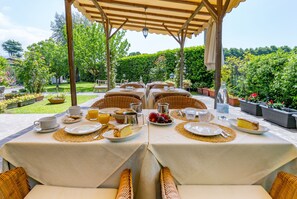 A dining area with tables set for breakfast, surrounded by lush greenery and a pergola. - B&B Miami Beach (Pietrasanta)