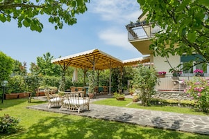 Un patio con mobiliario exterior, una zona de estar cubierta y un camino de piedra.